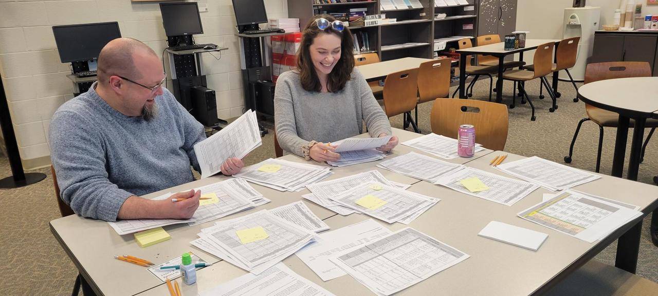 Patrick and Meredith sitting at a table covered in papers, smiling as they work on the schedule